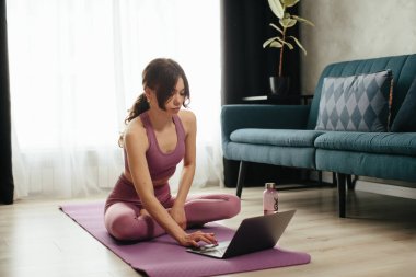 Yoga yapan çekici genç bir kadın evde yoga germe hareketleri yapıyor. Kişisel izolasyon internetteki yararlı, eğlenceli ve eğitimli bir şey. Sağlıklı yaşam tarzı kavramı.