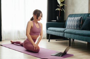 Yoga yapan çekici genç bir kadın evde yoga germe hareketleri yapıyor. Kişisel izolasyon internetteki yararlı, eğlenceli ve eğitimli bir şey. Sağlıklı yaşam tarzı kavramı.