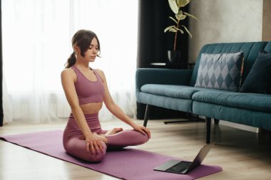 Yoga yapan çekici genç bir kadın evde yoga germe hareketleri yapıyor. Kişisel izolasyon internetteki yararlı, eğlenceli ve eğitimli bir şey. Sağlıklı yaşam tarzı kavramı.