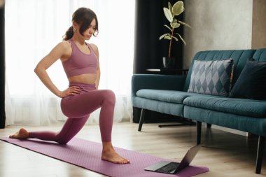 Yoga yapan çekici genç bir kadın evde yoga germe hareketleri yapıyor. Kişisel izolasyon internetteki yararlı, eğlenceli ve eğitimli bir şey. Sağlıklı yaşam tarzı kavramı.