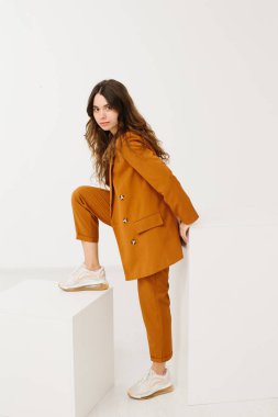 Beyaz arka planda küp üzerinde oturan modaya uygun pastel kıyafetli genç kadın.