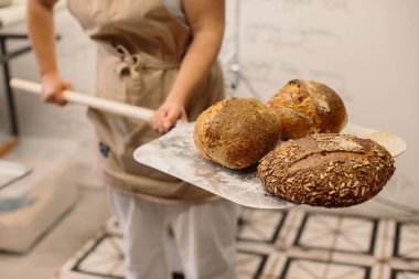 Fırında ekmek somununu soymak için kabuk kullanan bir fırıncı kadın.