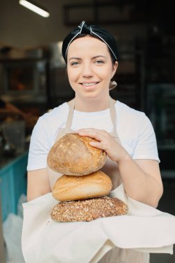 Vitrinin yanında kameraya gülümseyen neşeli bir fırıncının fotoğrafı. Fırınında taze ekmek, hamur işi ve fırın ürünleri satan kadın fırıncı ya da satıcı..