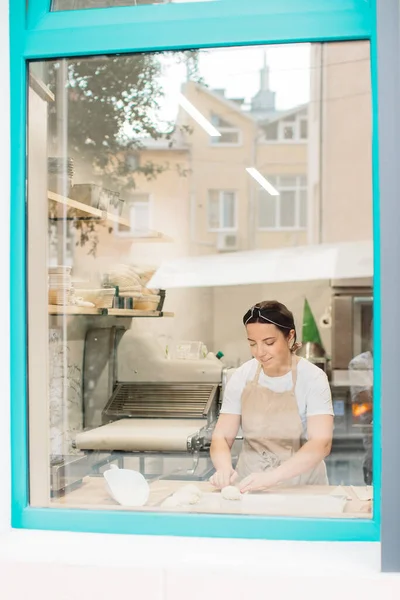 Woman baker making croissants in bakery standing in front of window.