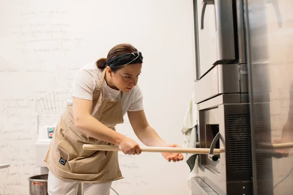 Female Baker Using Peel Take Out Loaf Bread Oven Bakery — ストック写真