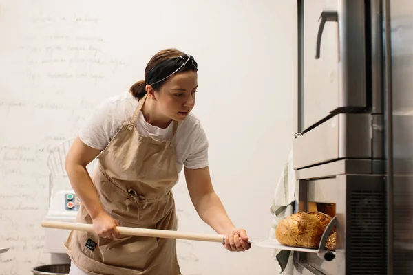 Female Baker Using Peel Take Out Loaf Bread Oven Bakery — ストック写真