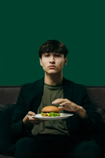 Young Man Green Stylish Suit Eating Burger While Sitting Sofa — ストック写真