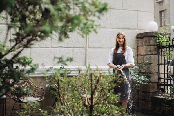 Woman watering fresh herbs growing at home vegetable garden. Gardener taking care of plants at the backyard of her house. Concept of sustainability and growing organic