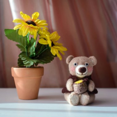 Oyuncak, el yapımı şirin ayı, bal fıçısının yanında oturuyor, sarı çiçeklerin yanında, yün gibi.