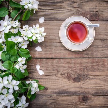 Bahar yerleşimi beyaz çiçeklerle çiçek açan bir elma ağacı dalı ve ahşap arka planda bir fincan çay