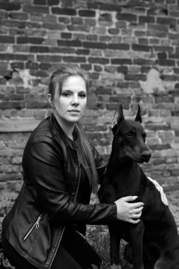 Deri giyen bir kız, bir dobermanla, eski bir avluda..