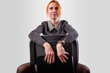 Business woman, legs wide apart, sits on a chair backwards, on a gray background