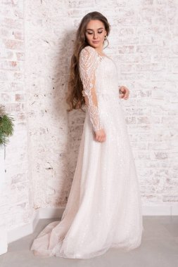 Beyaz elbiseli gelin tuğla duvara yaslanmış..