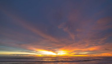 Denizin üzerinde günbatımında gökyüzünde renkli bulutlar renk değiştiriyor.
