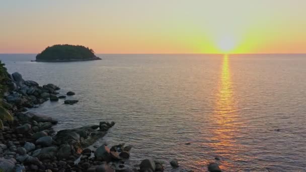 島の横の木々の上の夕日の地平線に沈む空の景色島の周りのいくつかのサイズの石でいっぱいの岩のビーチ海の背景の上の風景日没 — ストック動画