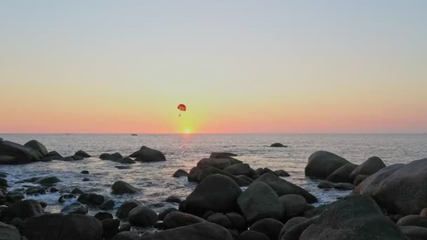 島の横の木々の上の夕日の地平線に沈む空の景色島の周りのいくつかのサイズの石でいっぱいの岩のビーチ海の背景の上の風景日没 — ストック動画