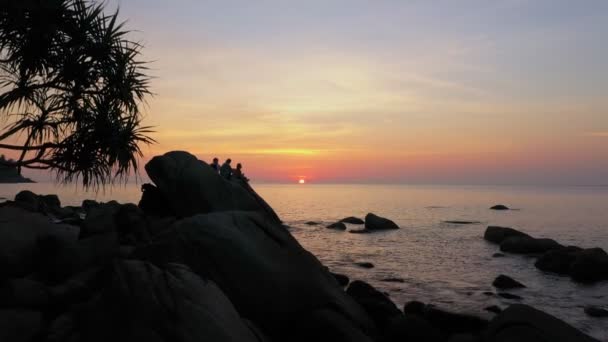 空の景色シルエットの観光客が夕日を見るために大きな岩の上に座っています 夕日の島の横にある美しい自然 — ストック動画