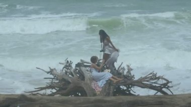 . A large pine root decay on the Mai Khao beach, .during the high tide it hits the logs. .Two women happily walked down to relax on the roots..4K. High quality video.