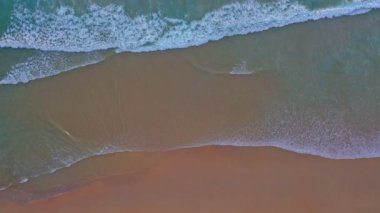 aerial top view sea waves seamless loop on the white sand beach. Wave after wave swept towards the shore. green sea, white bubble waves,and clear sand landscape. Paradise beach.