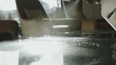 Bir otel çalışanı masanın cam yüzeyine dezenfektan sürer..