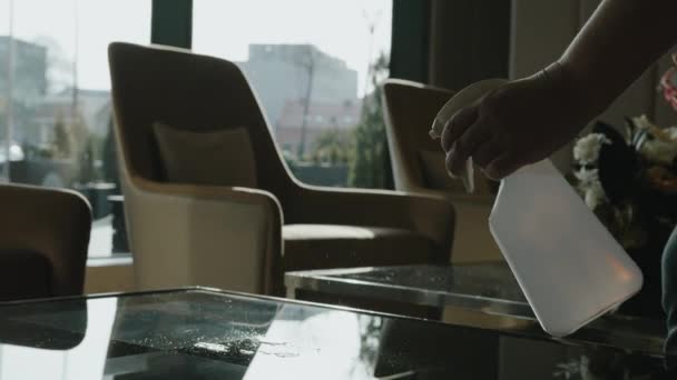 Een hotelmedewerker brengt desinfectiemiddel aan op het glazen oppervlak van de tafel. Stockvideo