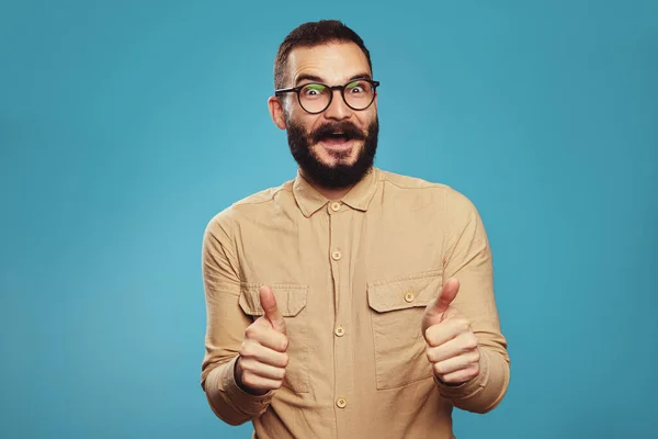 Varón con barba usando gafas y mostrando los pulgares hacia arriba felizmente en azul — Foto de Stock