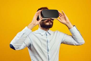 Sarı arka planda VR kulaklık takmış, sırıtan genç bir erkek.
