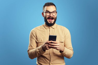 Şok olmuş adamın elinde cep telefonu var, zaferi kutluyor, mavi üzerinden izole edilmiş.