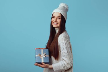 Büyük beden süveter ve şapka giyen, elinde hediye kutusu olan mutlu genç bir kadın.