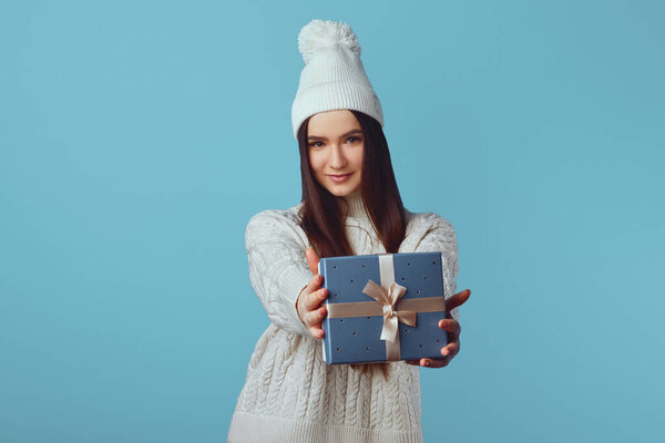 Cute excited woman in white sweater and hat holding gift present surprise