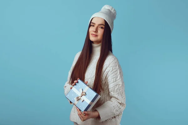 하얀 스웨터를 입고 파란 선물 함을 든 모자를 쓴 귀여운 여자 — 스톡 사진