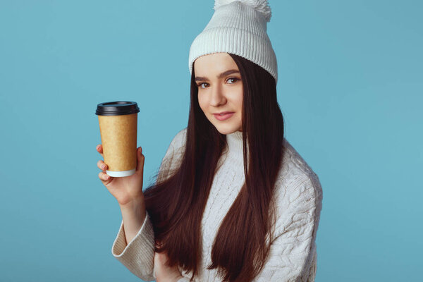 Caucasian happy woman wearing white sweater and hat, holding takeaway coffee