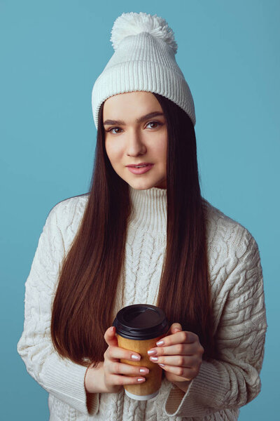 Girl wearing white hat and sweater, enjoys drinking coffee from takeout cup