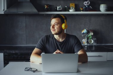 Kulaklıklı düşünceli bir erkek, kameraya bakarken gülümsüyor, müzik dinliyor.