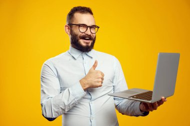 Genç adam yeni bir dizüstü bilgisayar tutuyor ve sarıya gülümserken başparmağını gösteriyor.