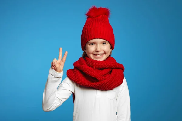 Chica con bufanda roja y sombrero, mirando a la cámara y mostrando gesto de paz — Foto de Stock
