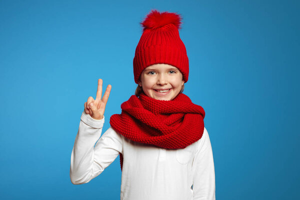 Girl wearing red scarf and hat, looking at camera and showing peace gesture