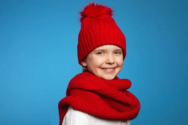 Piros sálat és kalapot viselő kislány, kamerába néz, kék felett elszigetelve. — Stock Fotó
