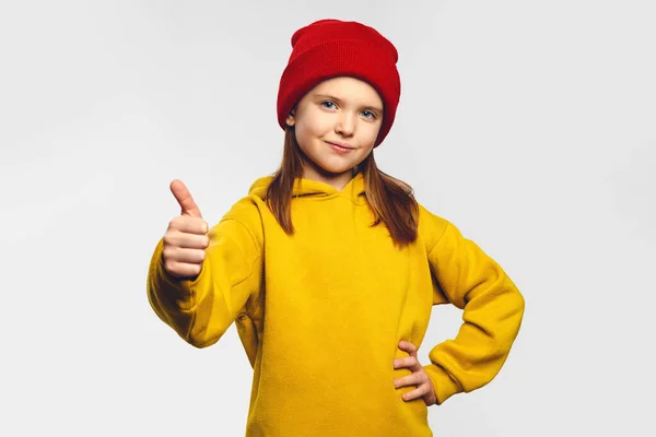 A lány felmutatja a hüvelykujját, egyetért valamivel, mint a gesztus, sárga kapucnit visel. — Stock Fotó