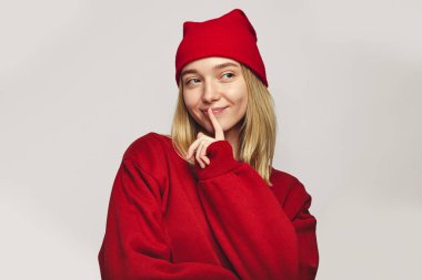 Sevimli kız nazikçe gülümser, işaret parmağını dudaklarında tutar, gizemli bir şekilde yana bakar.