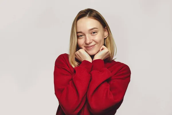 Молода жінка в червоному светрі позитивно посміхається, тримає підборіддя обома руками — стокове фото