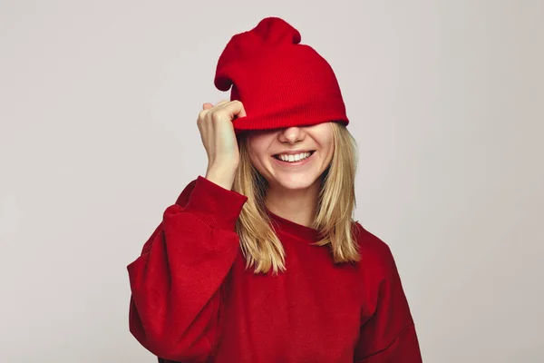 Boldog arctalan nő elrejti a szemét piros kalap visel pulcsi, úgy érzi, boldog — Stock Fotó