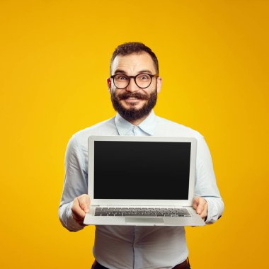 Gözlüklü ve bej gömlekli sakallı adam yeni modern laptop cihazını gösteriyor.