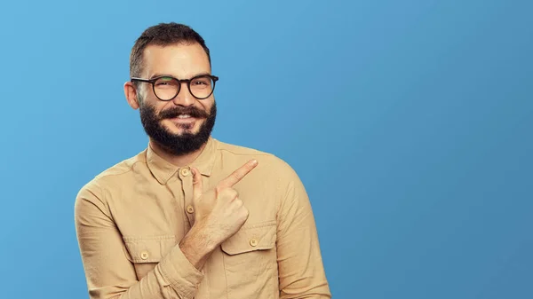 Empresário barbudo animado sorrindo enquanto aponta para o espaço vazio sobre azul — Fotografia de Stock