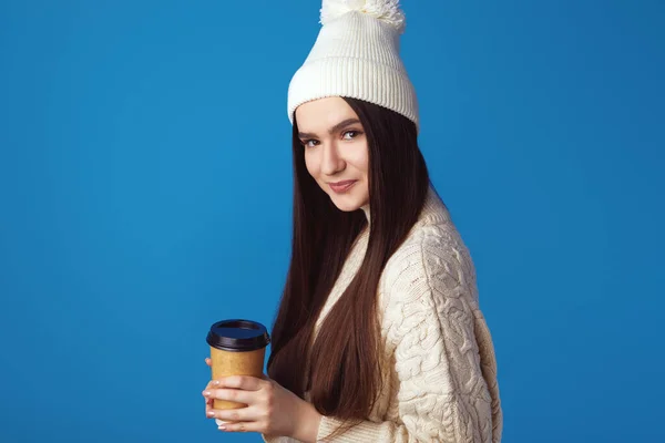 Молода весела дівчина в білому светрі і капелюсі, тримає каву на виході — стокове фото