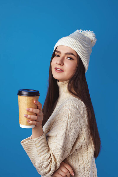 Girl wearing white hat and sweater, enjoys drinking coffee from takeout cup