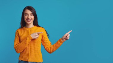 Güzel genç kadın iki işaret parmağıyla boş mavi alanı işaret ediyor.