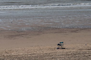 Deniz kıyısında kumlu bir sahilde tek başına bir sandalye.