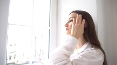 4K Güzel esmer kadın pencereden dışarı bakıyor.