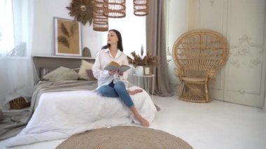 4k Carefree woman sitting on bed at home and reading book. 